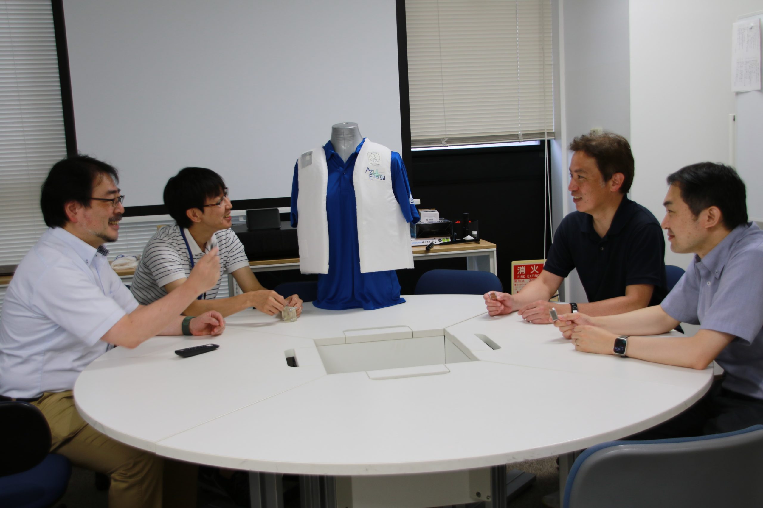 From left to right: Prof. Yabu, Mr. Ishibashi, Prof. Ono, and Mr. Ito discussing application of a metal-air paper battery to a smart life jacket equipped with a GPS sensor.